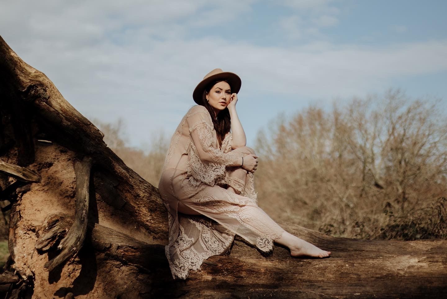 A person in vintage attire sits contemplatively on a fallen log in an autumn landscape.