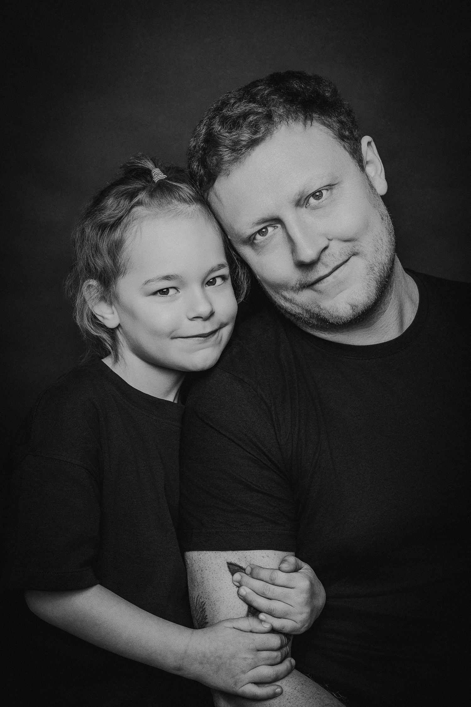 Black and white portrait of a parent and child embracing and smiling at the camera against a dark background.