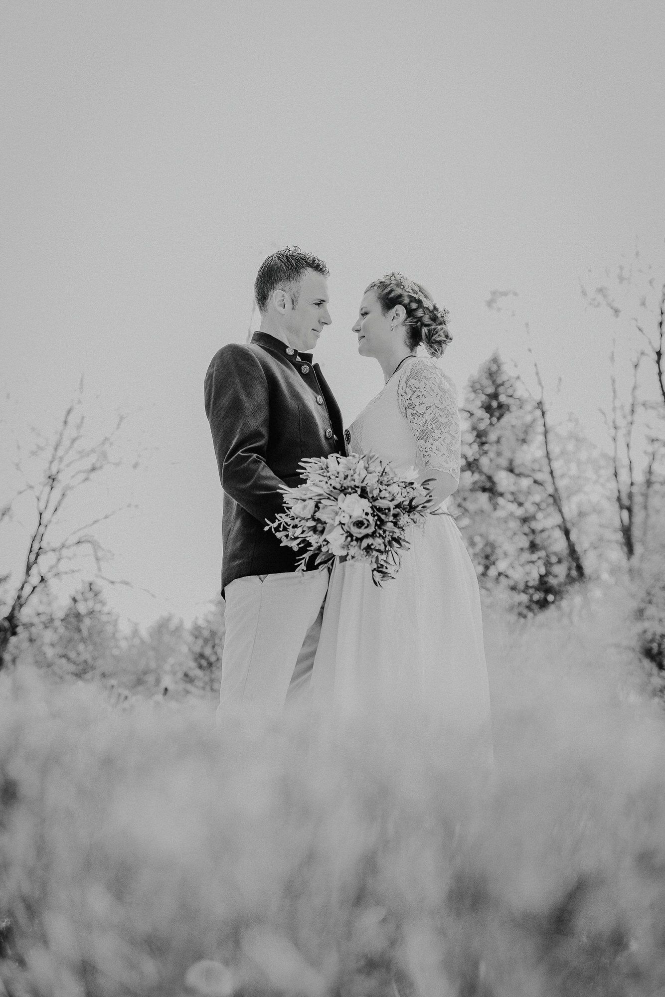 Black and white artistic wedding photograph showing couple embracing in a misty field with delicate wildflowers.