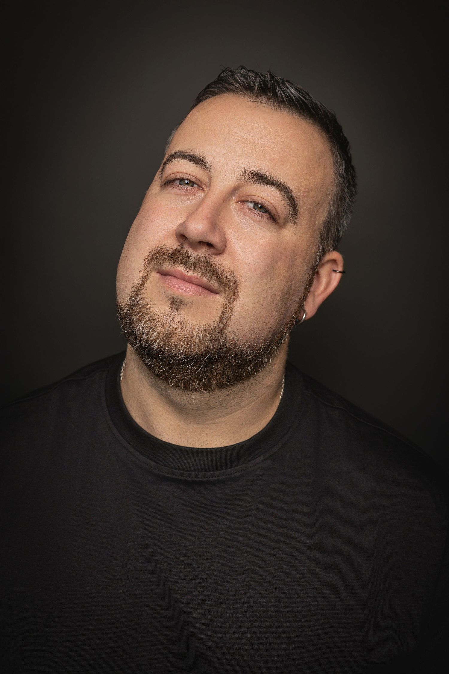 Professional headshot portrait of a person with facial hair wearing a black shirt against a dark background.