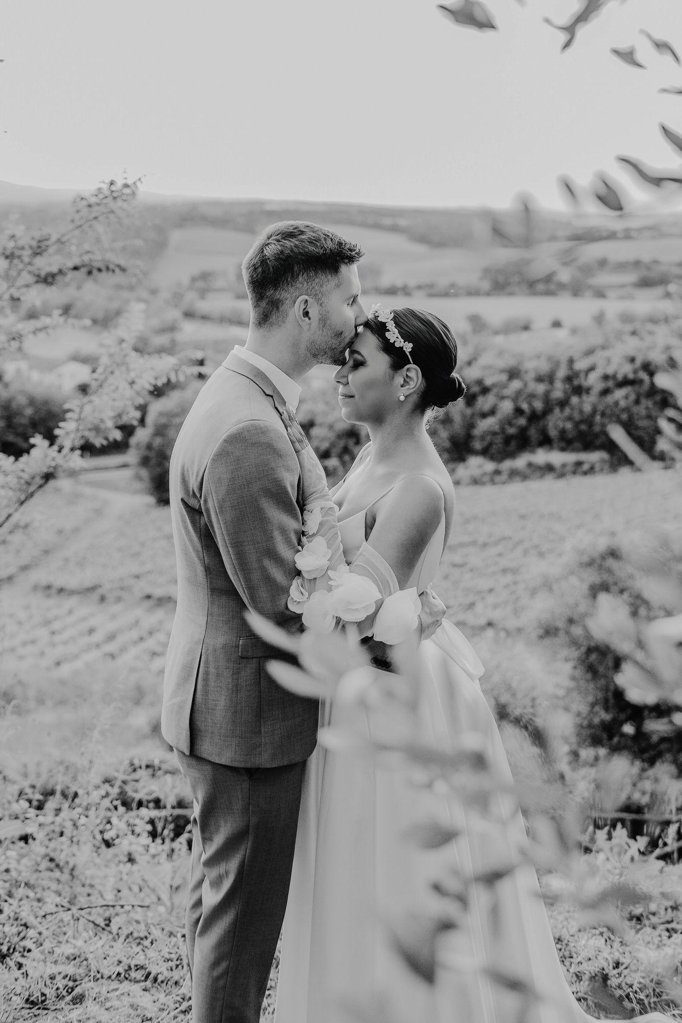 A romantic black and white wedding photo series showing a couple embracing outdoors against a scenic mountain landscape.
