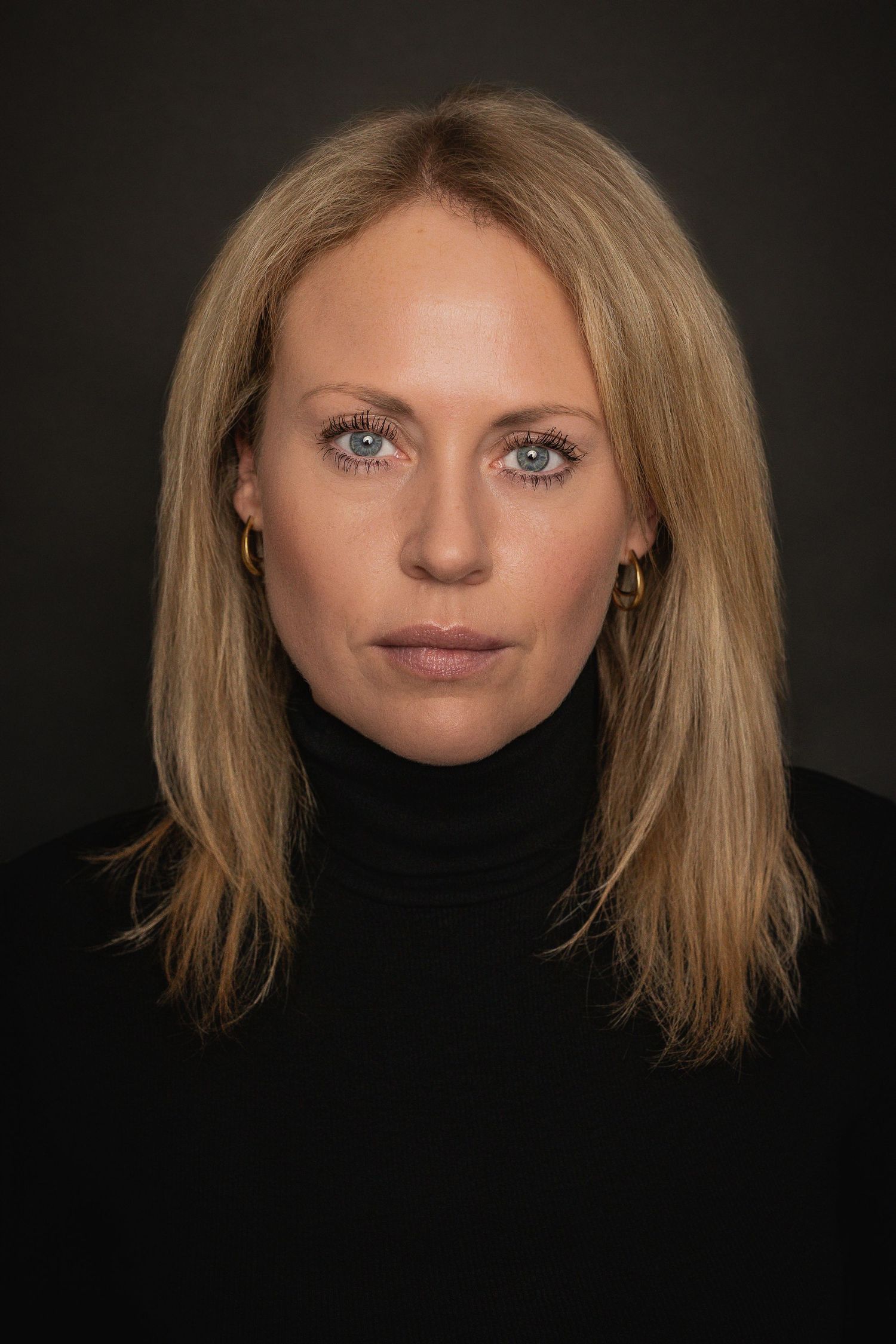 Pure Portrait vor dunklem Hintergrund mit blondem Haar und schwarzem Rollkragenpullover in reduzierter Beleuchtung.