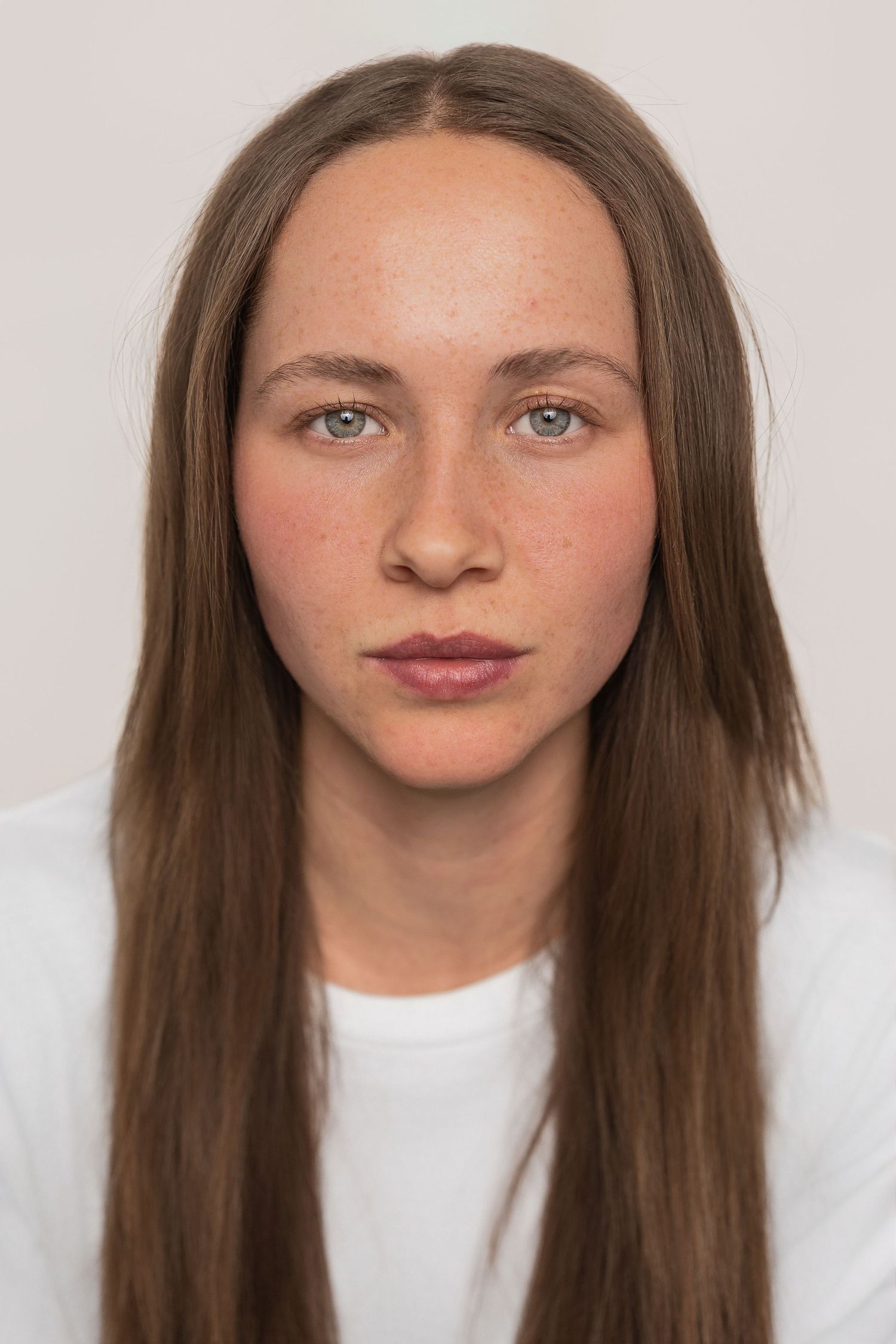 Portrait of a person with long brown hair wearing a white shirt against a light background.