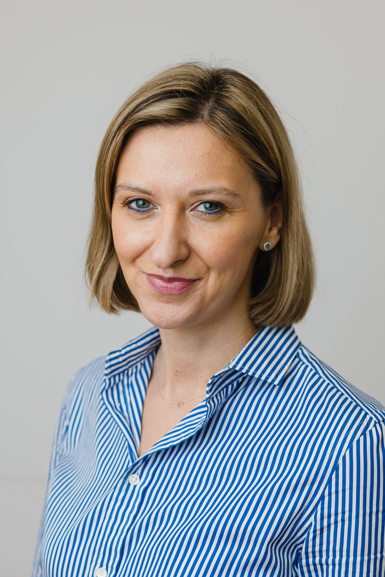 Professional headshot of a person wearing a blue and white striped button-up shirt against a light gray background.