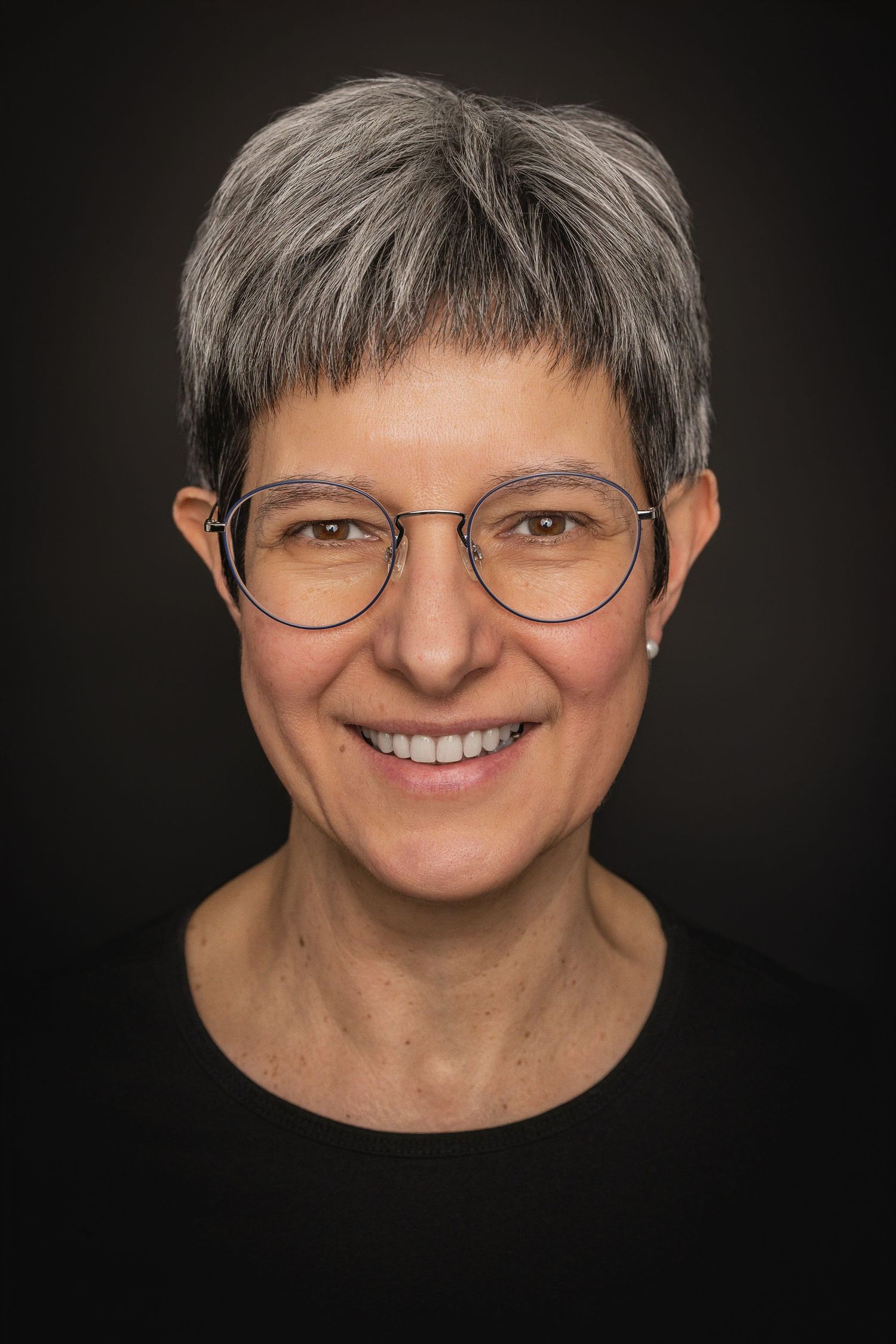 A series of five portrait photos against a black background showing warm smiles and round glasses.