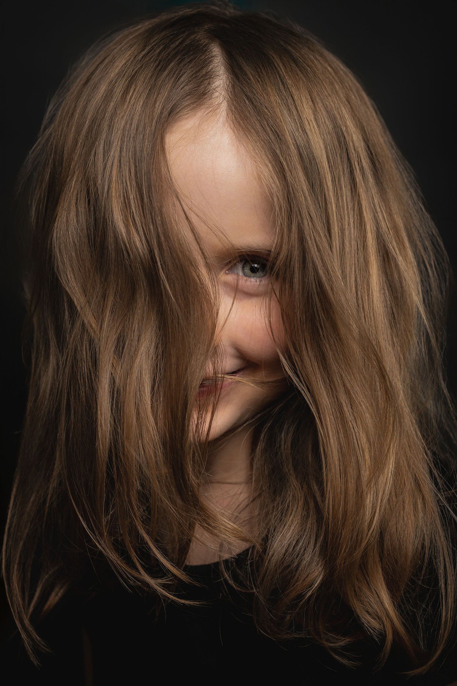 Dramatic portrait with light brown hair falling across face against dark background in moody lighting.