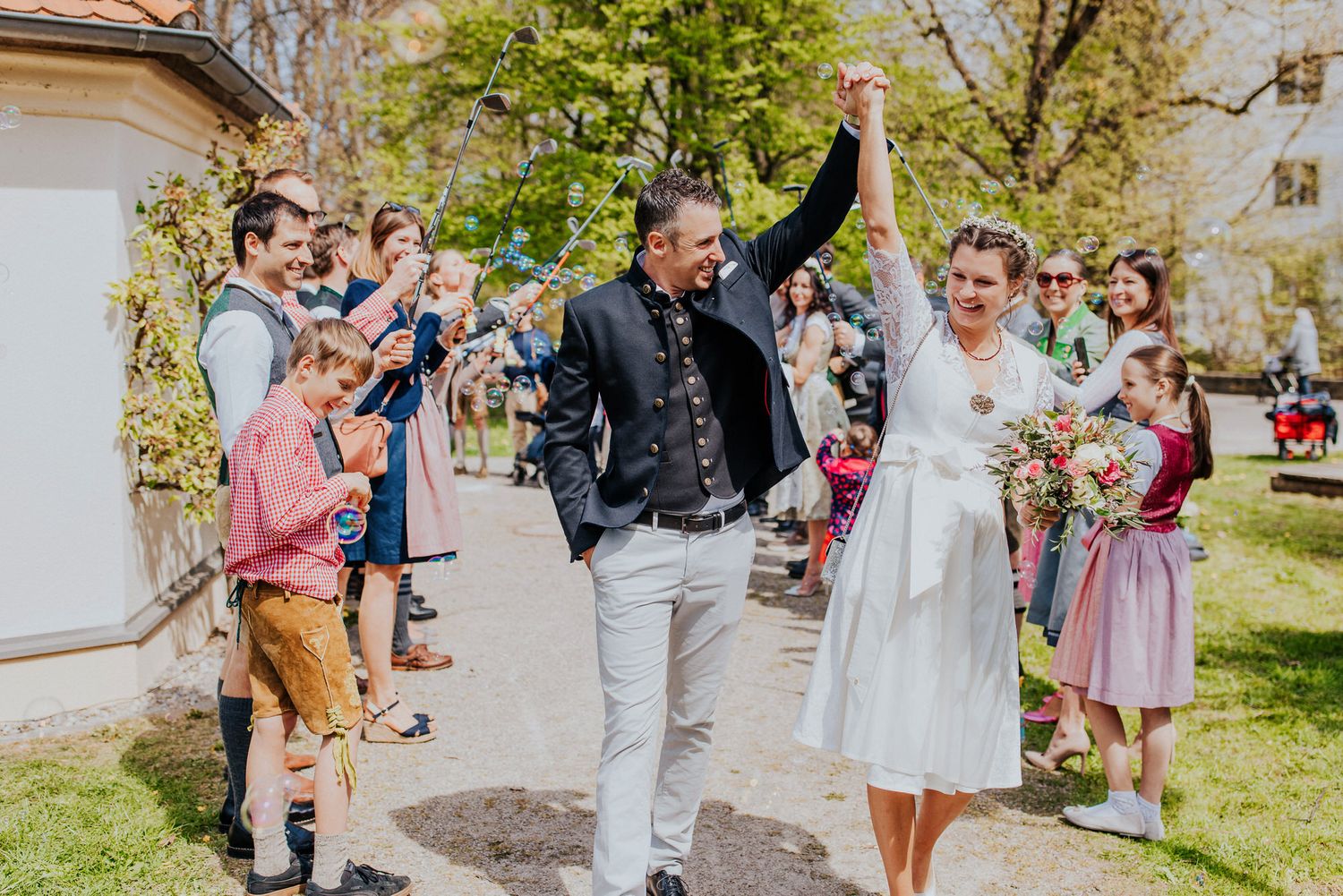 Guests gather outside a rustic stone building for a spring celebration with pink and white floral decorations.