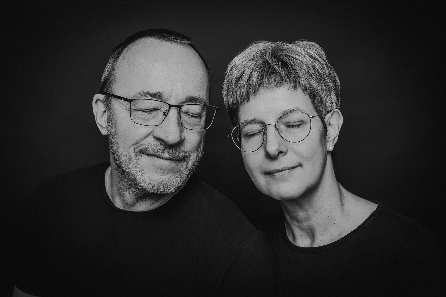 Schwarz-Weiß-Porträtserie, die Menschen mit Brille und Gesichtsbehaarung zeigt, die vor dunklen Hintergründen lächeln.