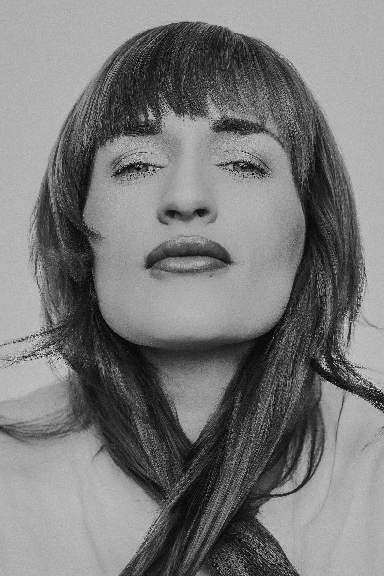 Black and white portrait photograph showing dramatic lighting on a person with long dark hair and bangs looking upward.