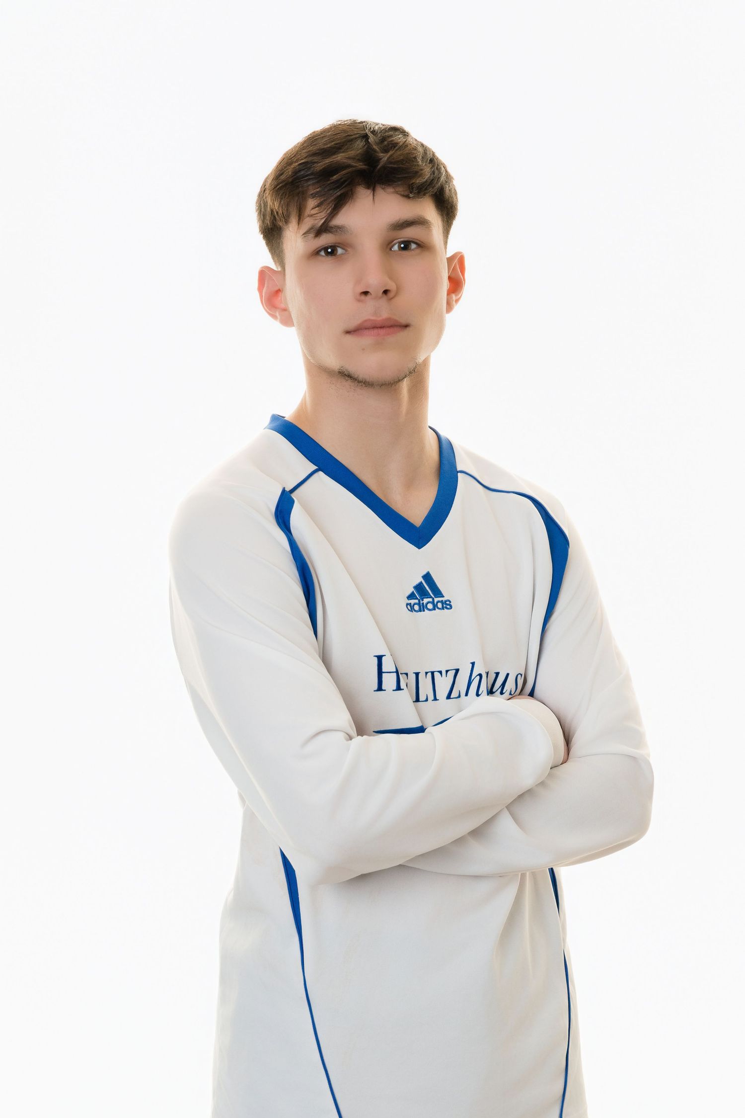 Young athlete in white Adidas cricket sweater with blue trim poses with arms crossed against white background.