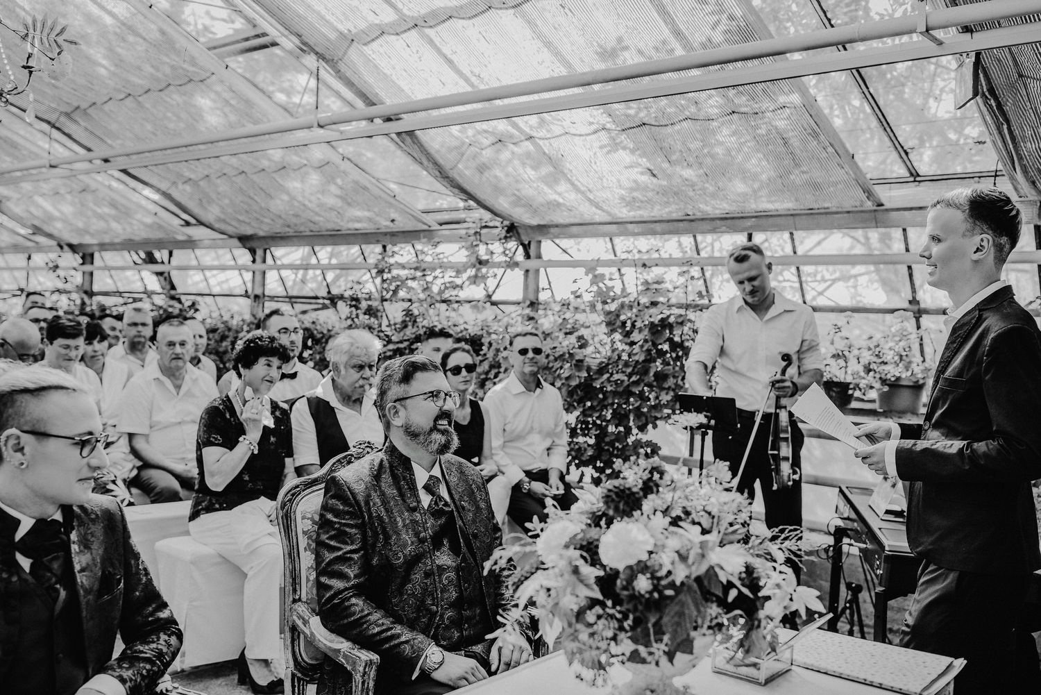 Wedding guests gather under a clear tent canopy during an outdoor reception celebration.