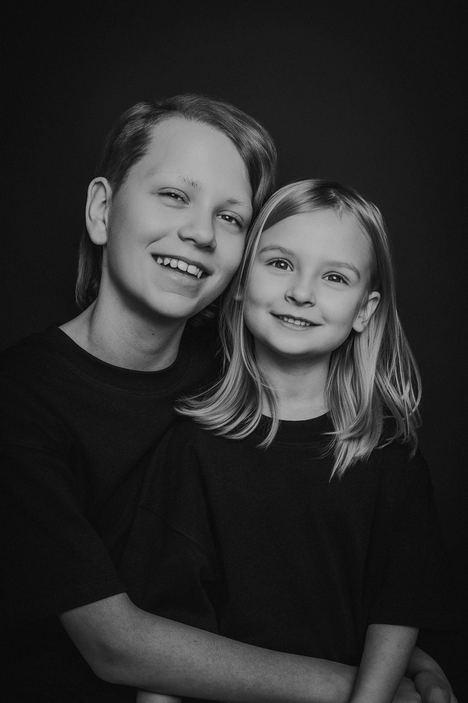 Schwarz-Weiß-Studioporträt von zwei Kindern in passenden dunklen Hemden vor dunklem Hintergrund.