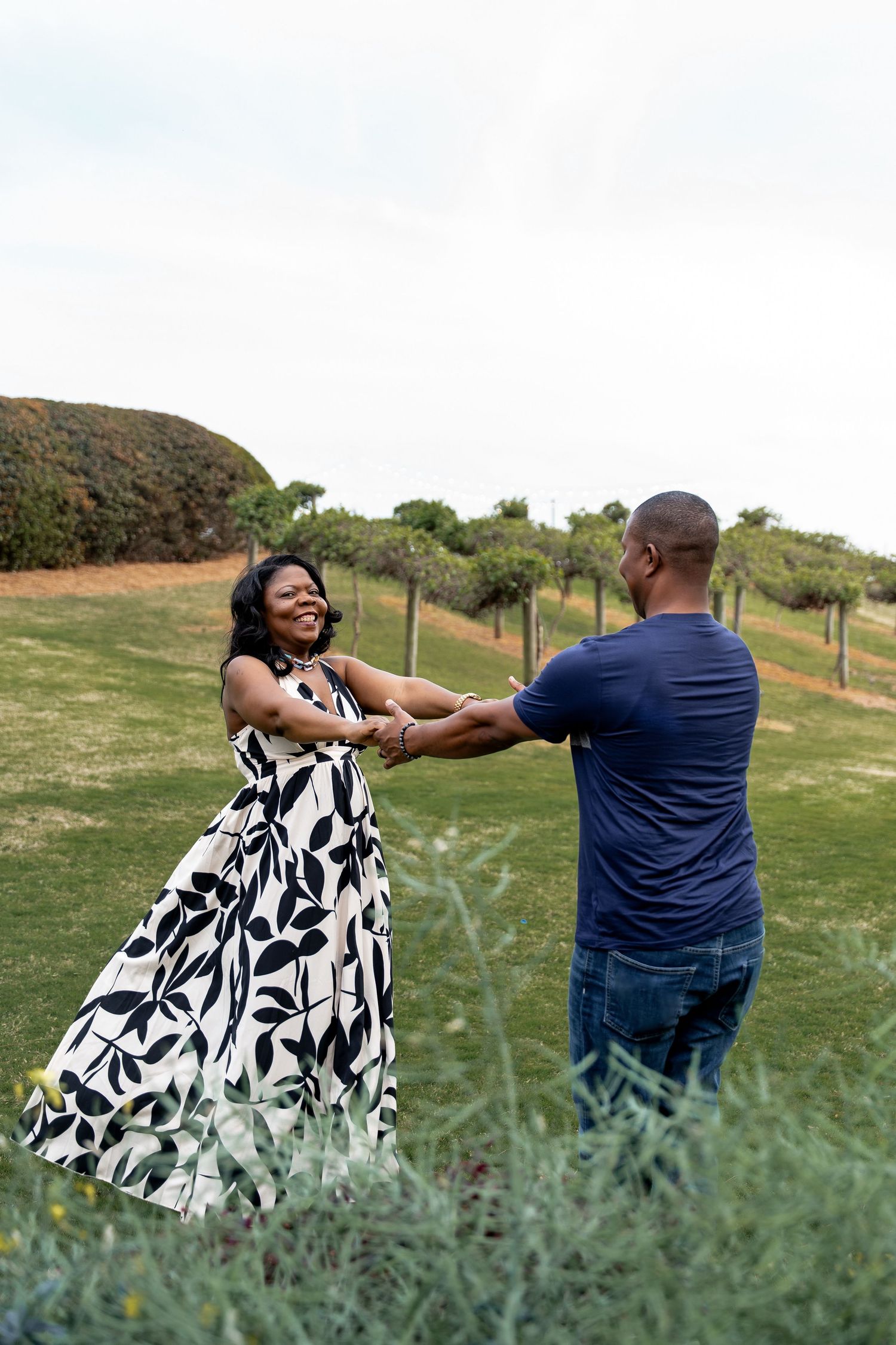 A couple in a grassy field shares candid moments together, with one wearing a black and white patterned dress.