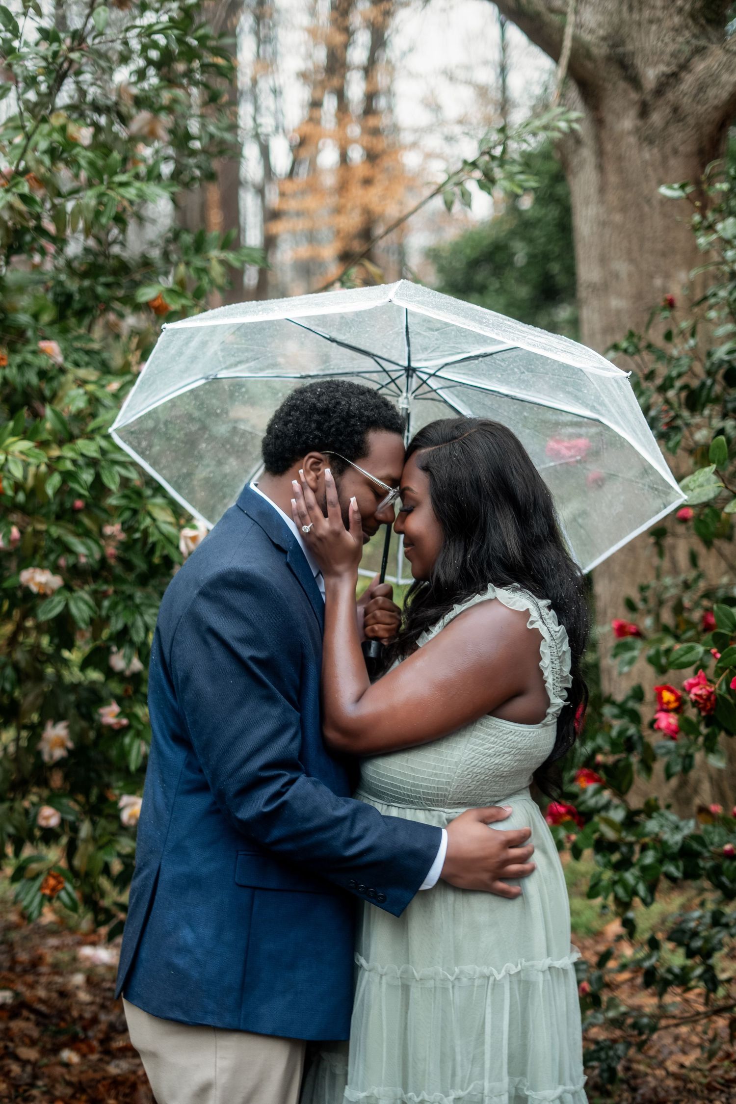 A romantic couple shares an intimate moment under a clear umbrella surrounded by autumn foliage.