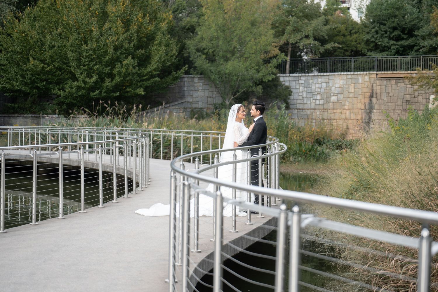 Metal handrails along a curved concrete path lead through a green landscaped area on a sunny day.
