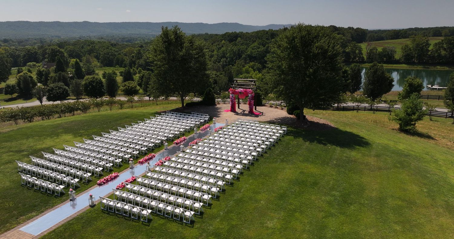 Aerial view of white chairs arranged outdoors for a scenic wedding ceremony with a red gazebo at the end of the aisle.