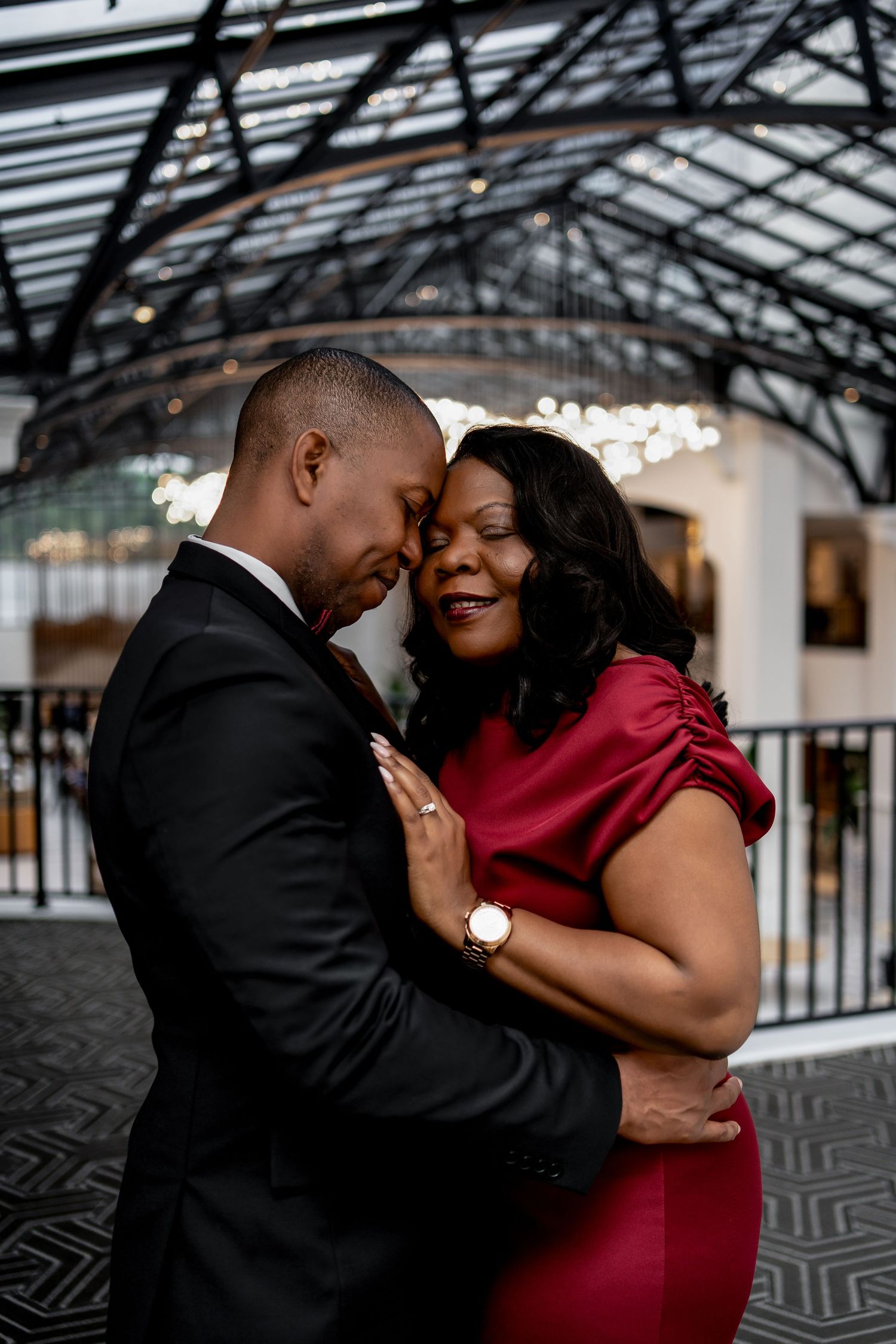 A romantic couple embraces in an elegant indoor venue with glass ceiling and geometric floor pattern.