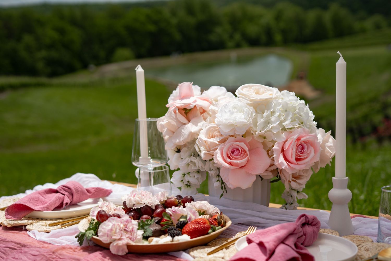 Romantic outdoor table setting with pink roses, white candles and fresh berries on a pink linen tablecloth.