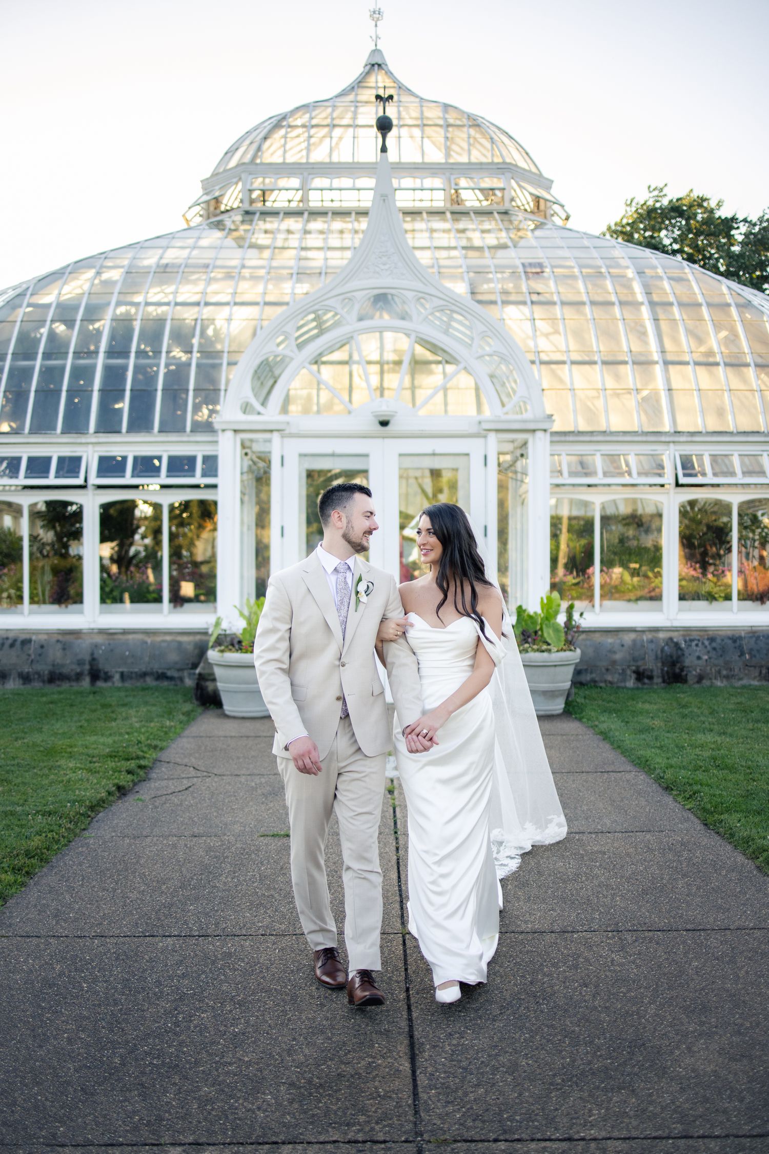 Bride and groom holding hands in front of a stunning glass greenhouse conservatory on their wedding day.