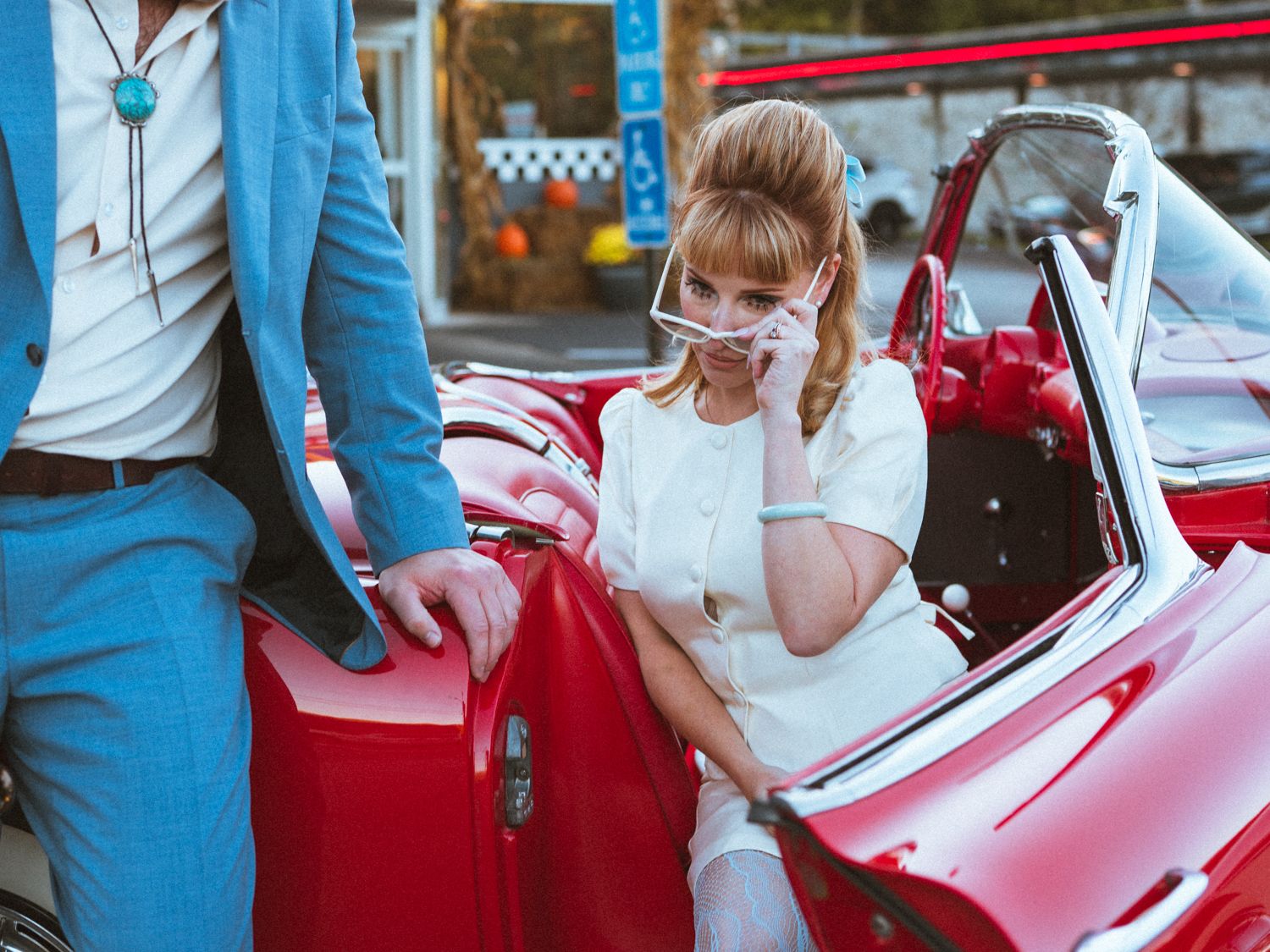 Close-up view of someone in a red dress sitting in a pink vintage convertible car.