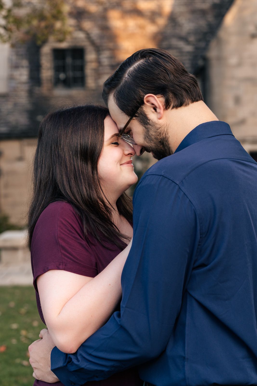 A romantic couple embraces outdoors, sharing an intimate moment in front of a stone building.