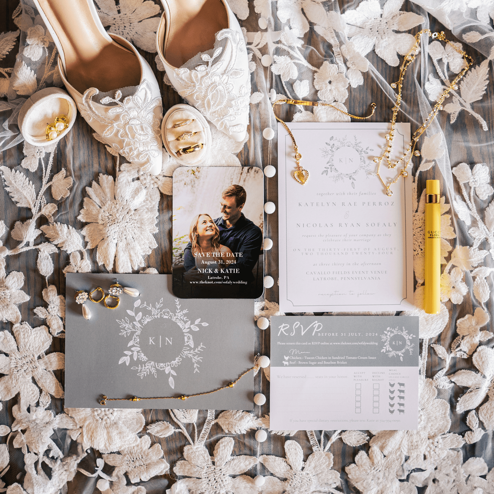 Elegant wedding flat lay with lace bridal shoes, floral invitations, RSVP cards, gold jewelry, and yellow perfume on lace fabric.