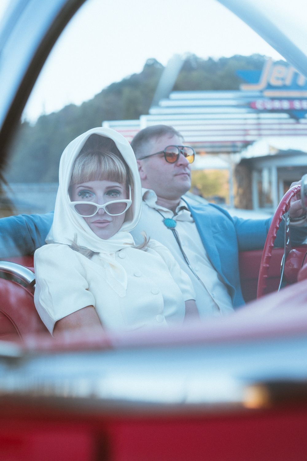 Stylish couple in retro sunglasses enjoying a ride in a classic red convertible car on a sunny day.