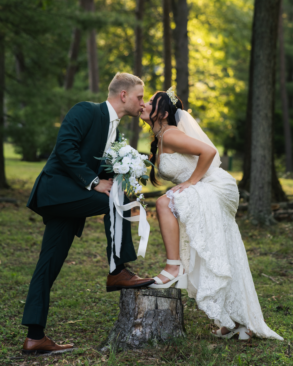 Bride and groom sharing a kiss on a tree stump in a forest during their outdoor wedding photo session.