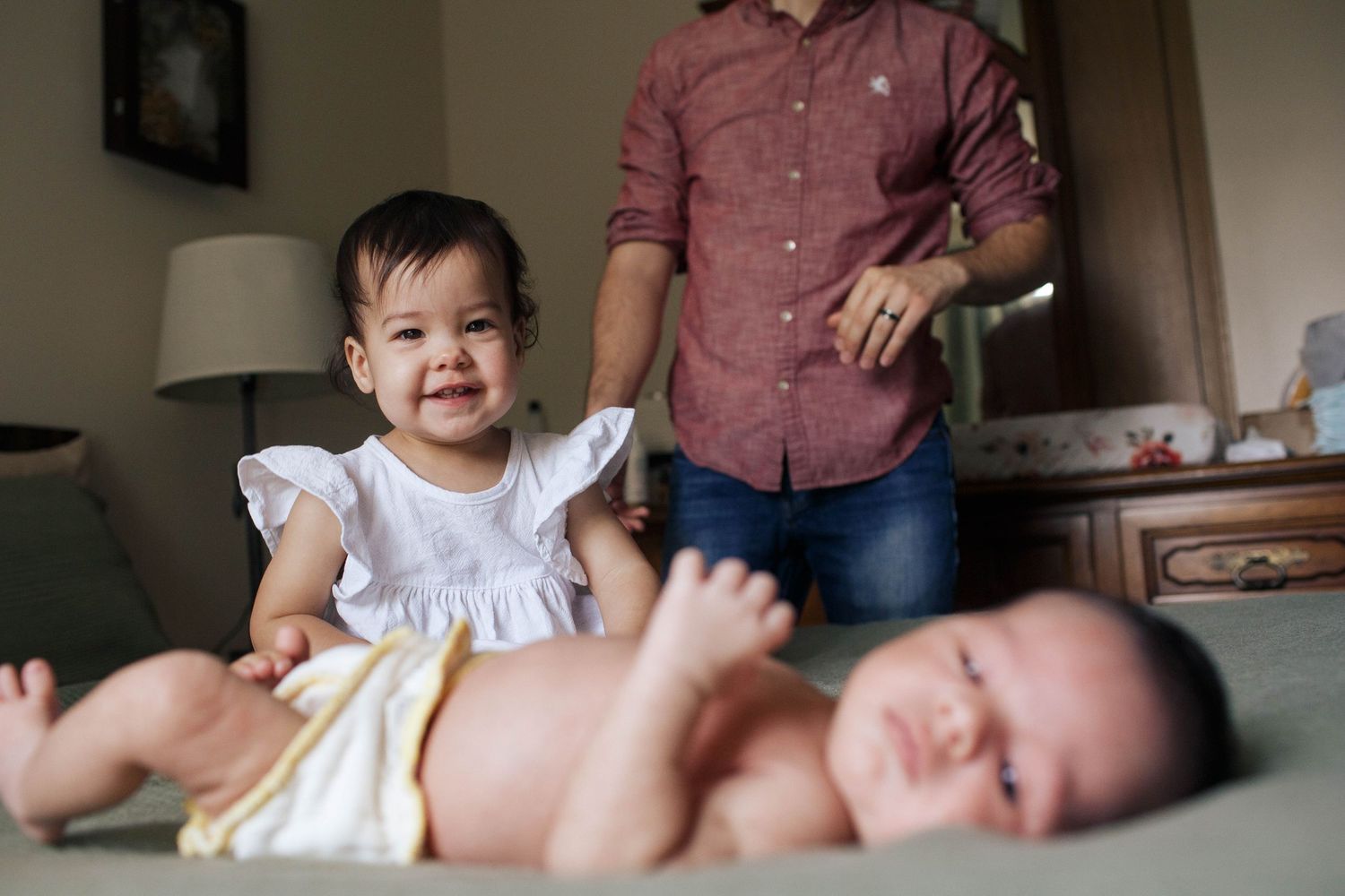A toddler looks over at her newborn baby brother in natural light during an indoor newborn photo session in Everett WA
