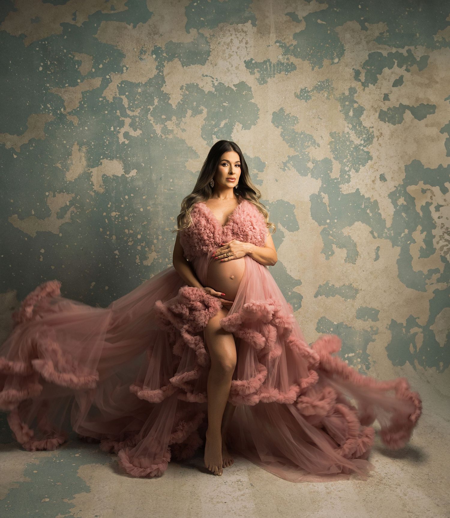A flowing dusty rose tulle gown creates an ethereal effect against a distressed vintage wall backdrop.