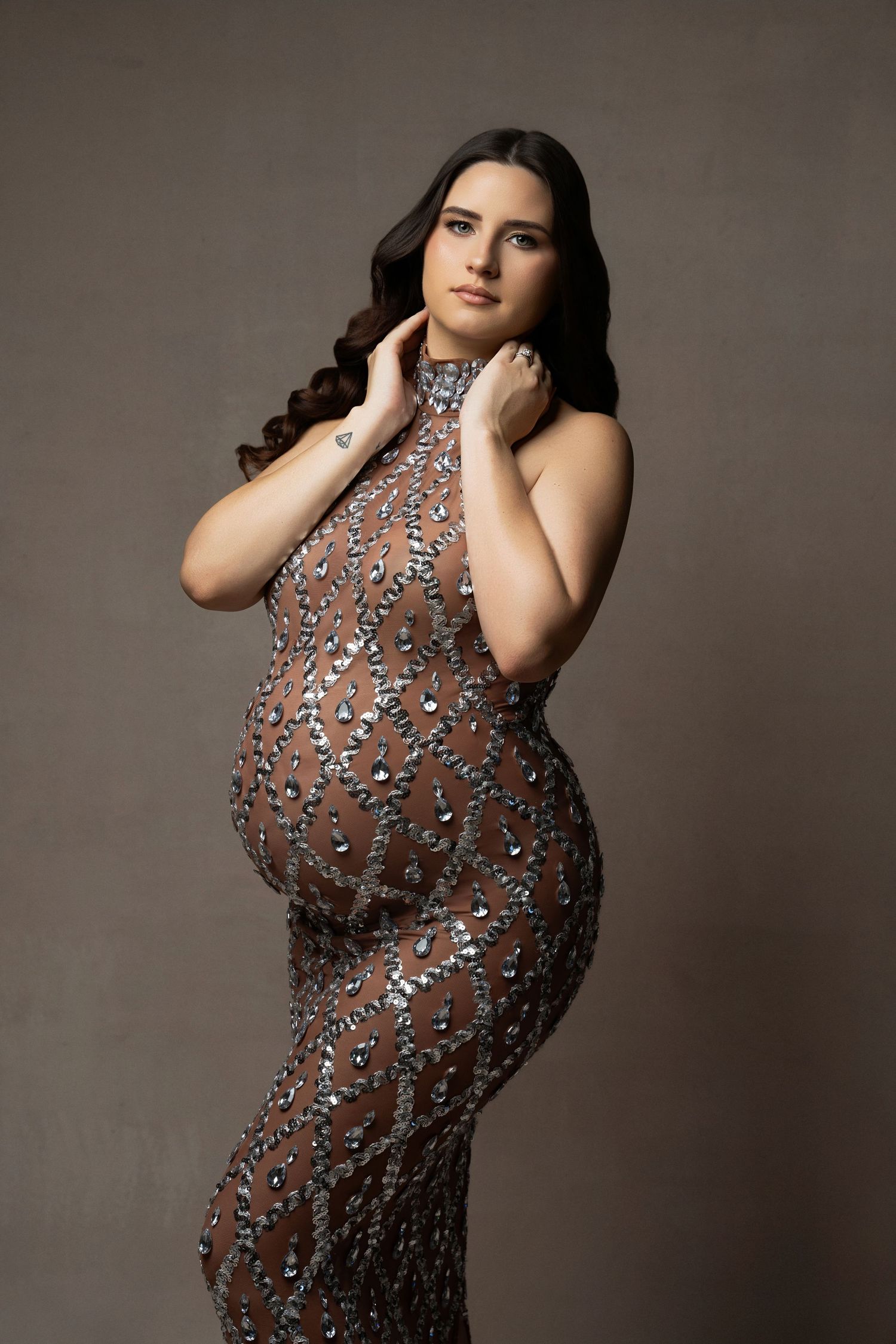 Fashion model poses in a sleek sheer gown adorned with sparkling silver embellishments against a neutral backdrop.