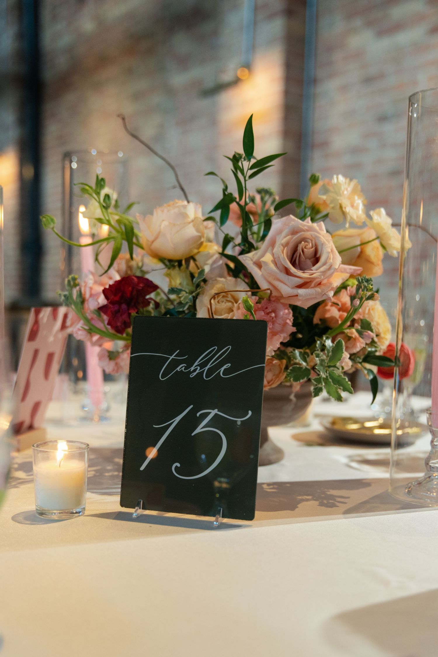 Elegant wedding table setting with table number 15 displayed on black card alongside pink roses and lit candles.