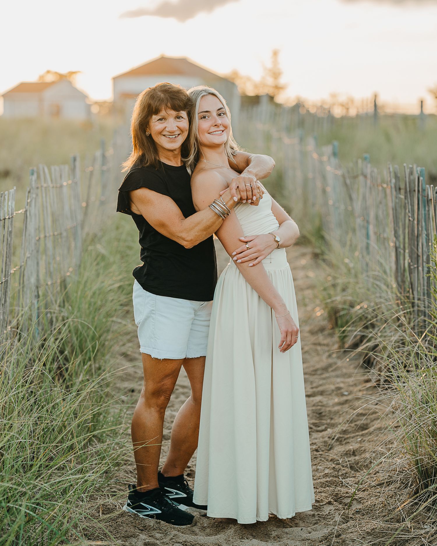 Two people share a tender moment together in a field of tall grass during golden hour sunset.