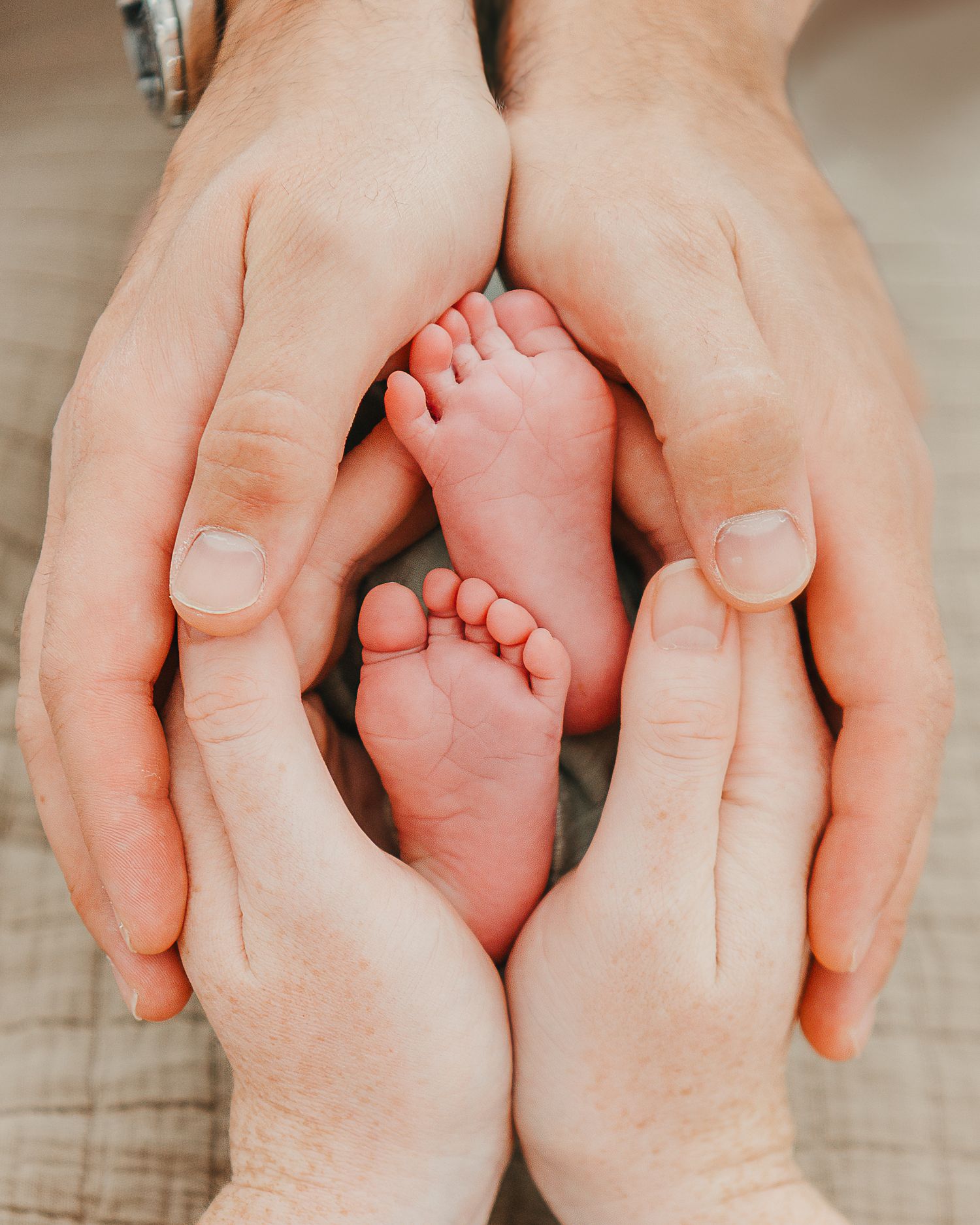 Adult hands gently cradling tiny newborn baby foot against soft fabric background.