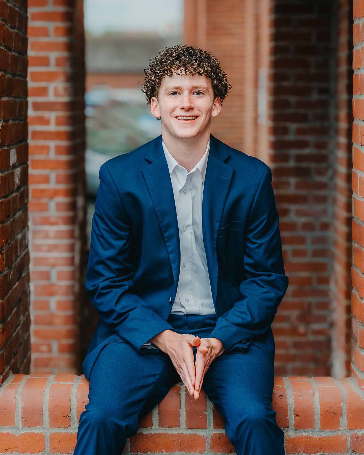 Person in navy blue suit sitting on brick steps smiling at the camera in an outdoor setting.
