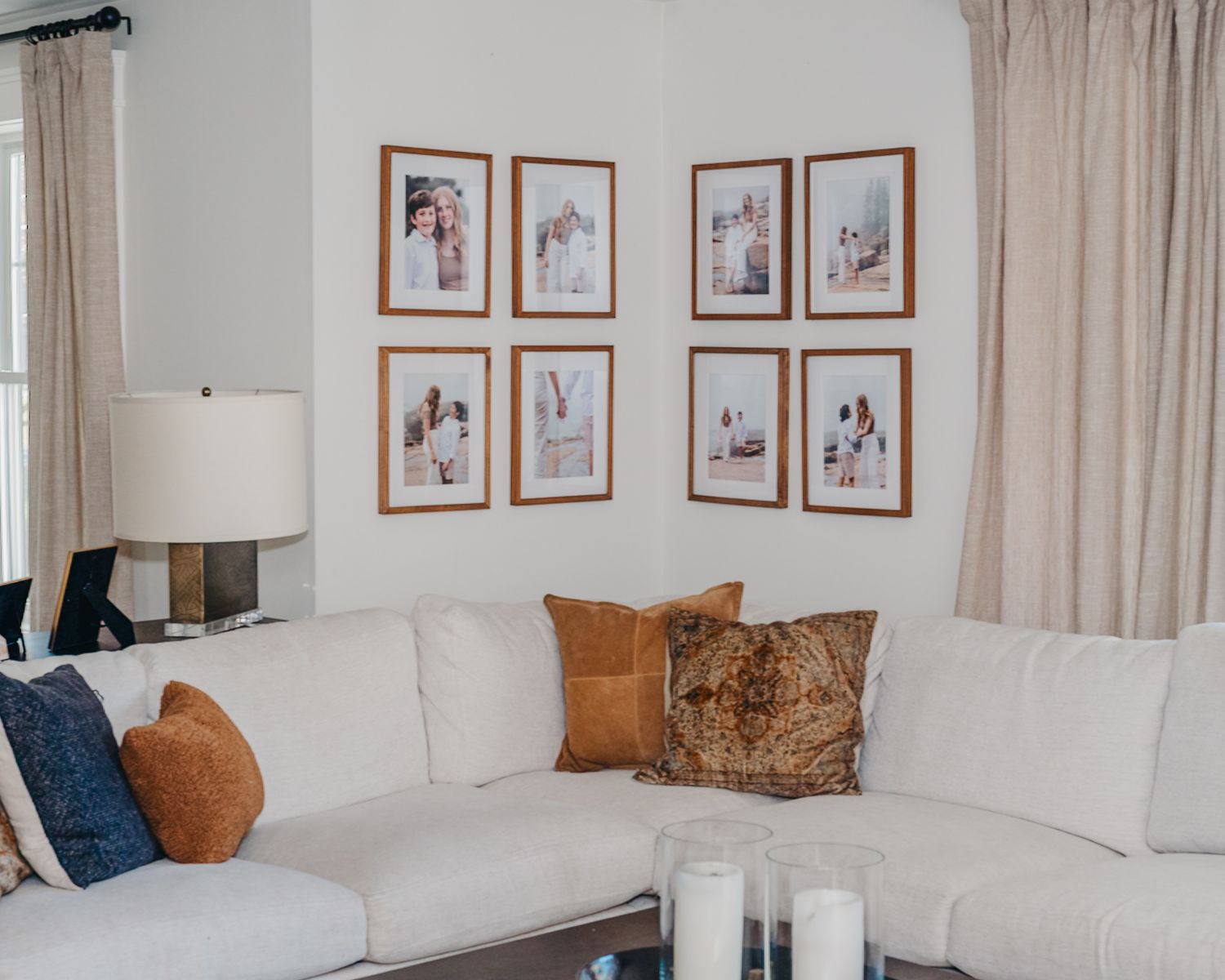 Modern living room with white sectional sofa, orange accent pillows, and framed artwork on beige walls.