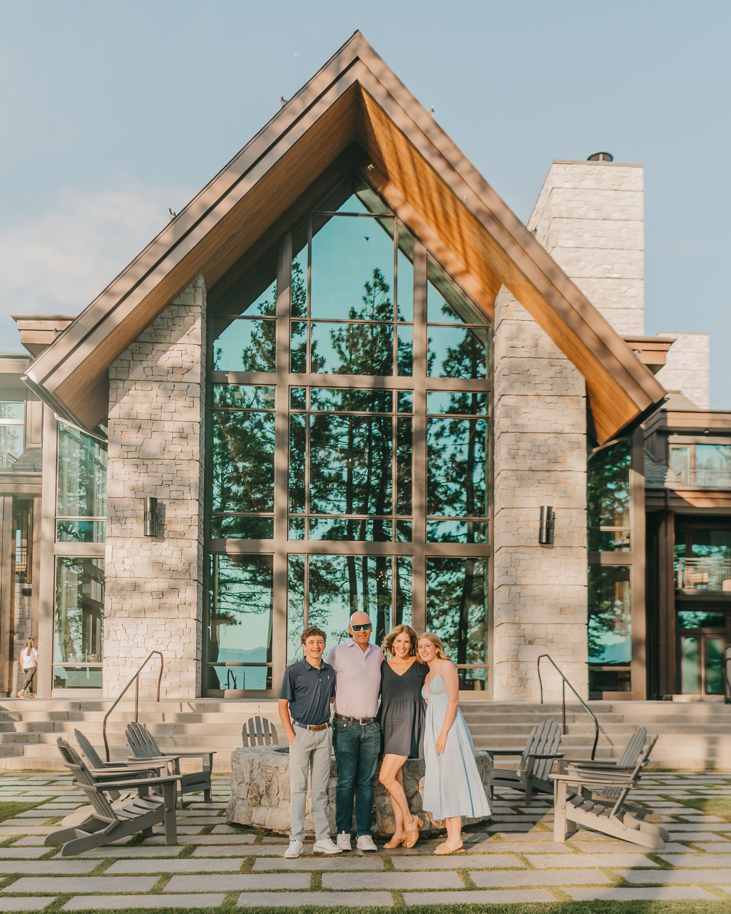 Three people posing in front of a stunning modern lake house with floor-to-ceiling glass windows and stone facade.