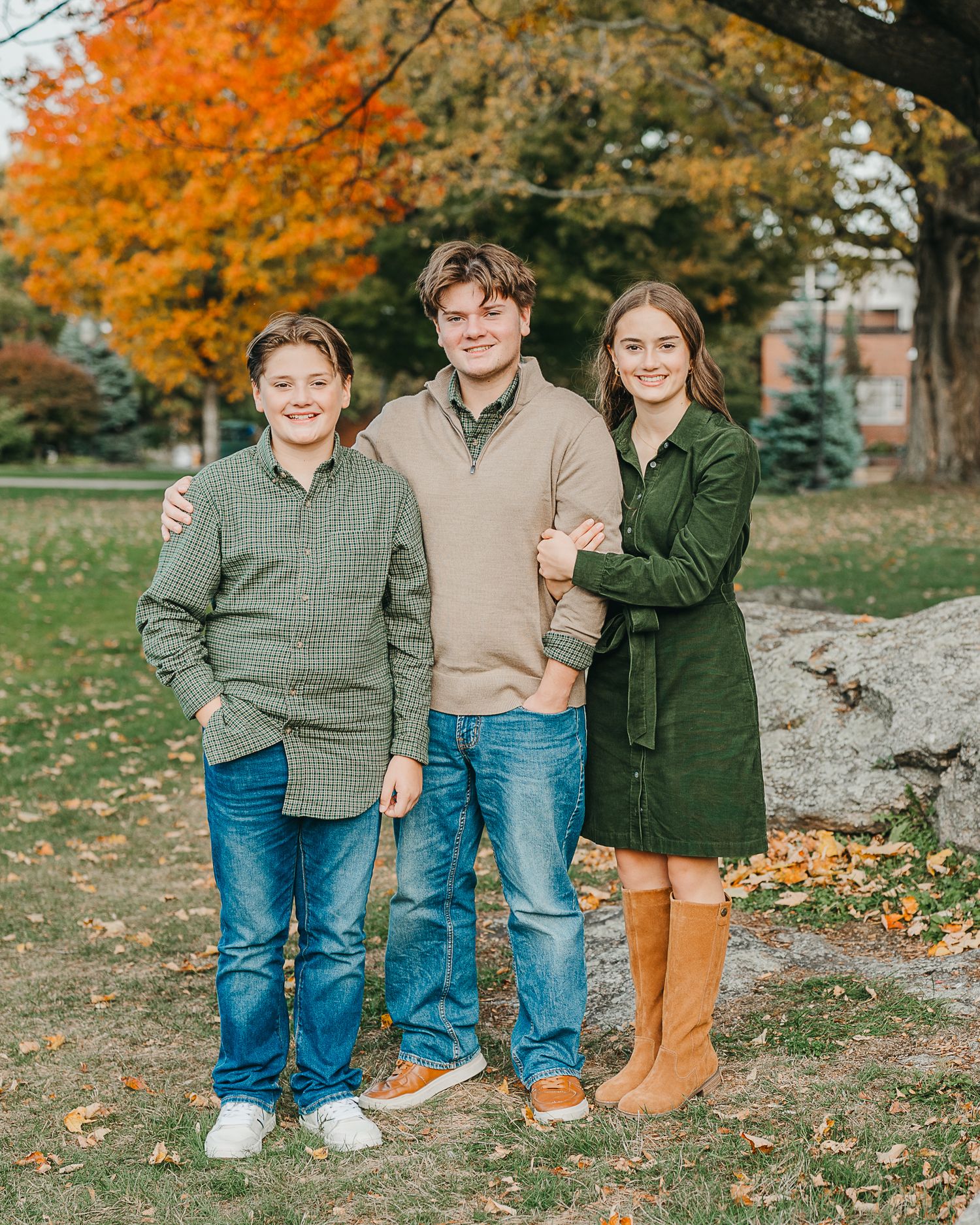 Three people standing together outdoors with vibrant orange autumn foliage in the background.
