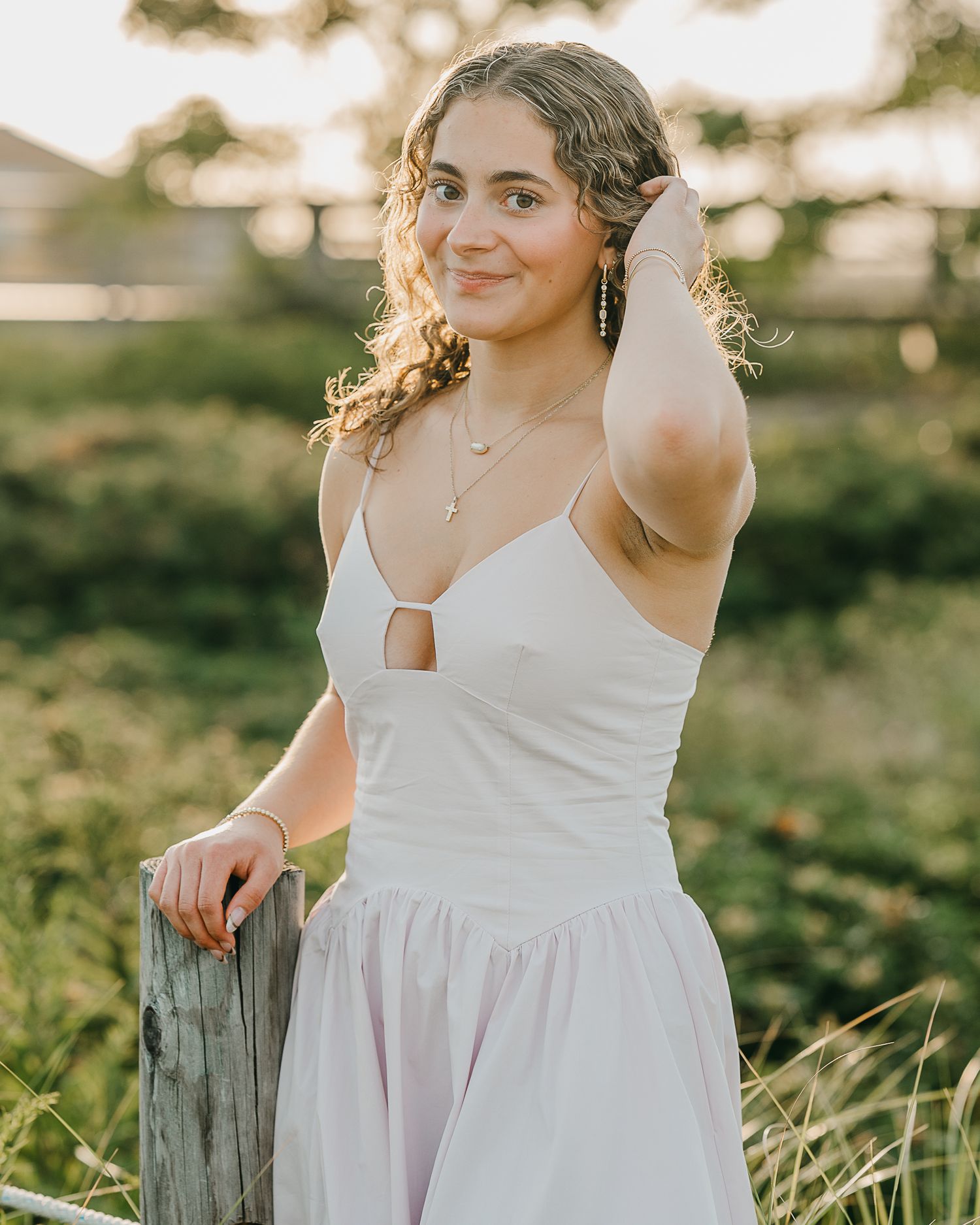 A person in a white summer dress poses in a sunlit field with golden bokeh effects in the background.