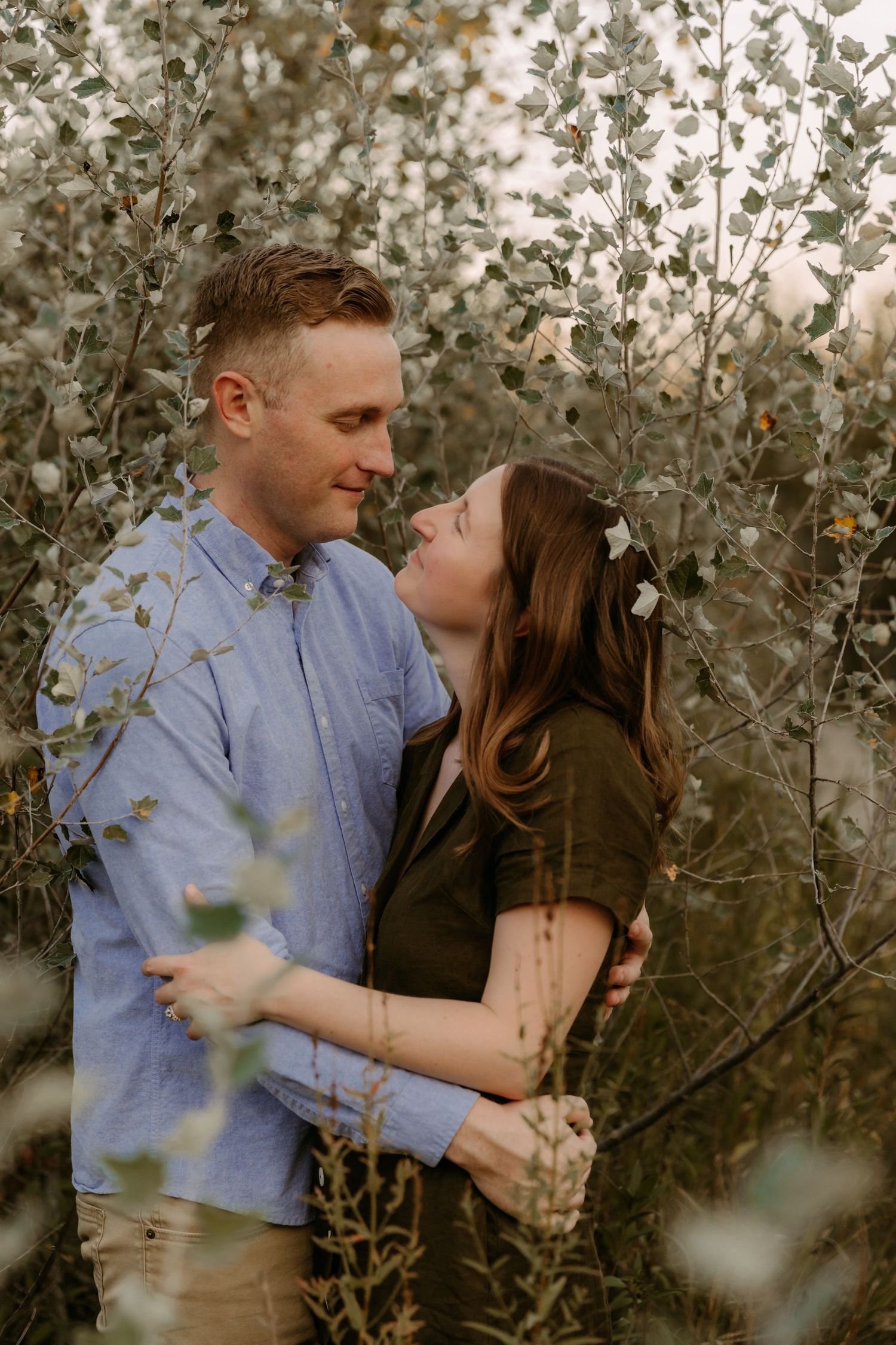 Romantic couple embraces among flowering branches in soft natural lighting.
