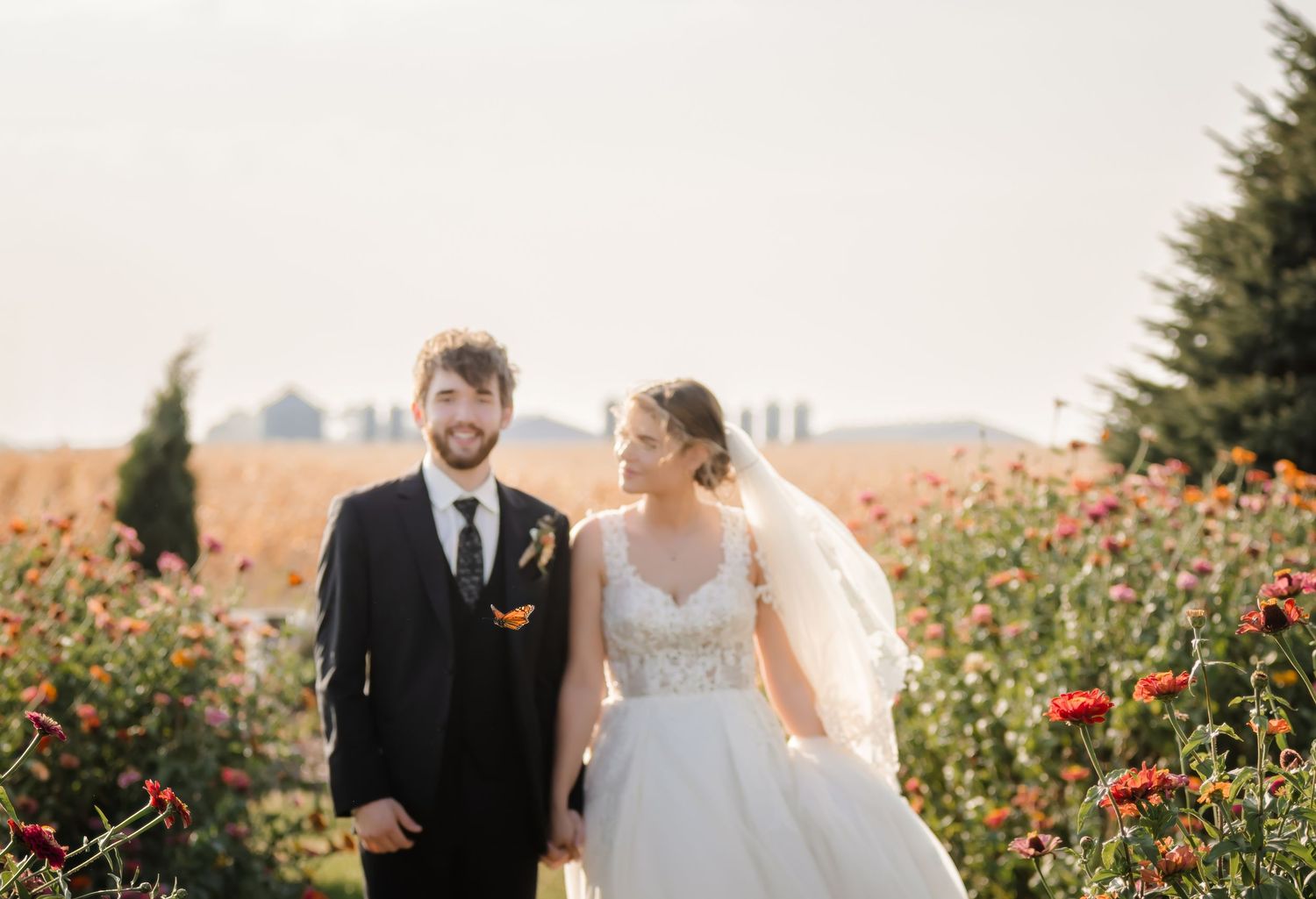 A newlywed couple stands together in a vibrant field of red poppies during golden hour.