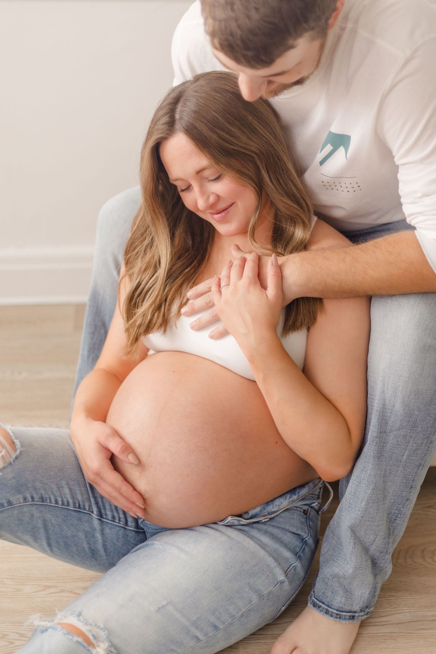 Intimate maternity photo of expecting couple sitting on wooden floor.