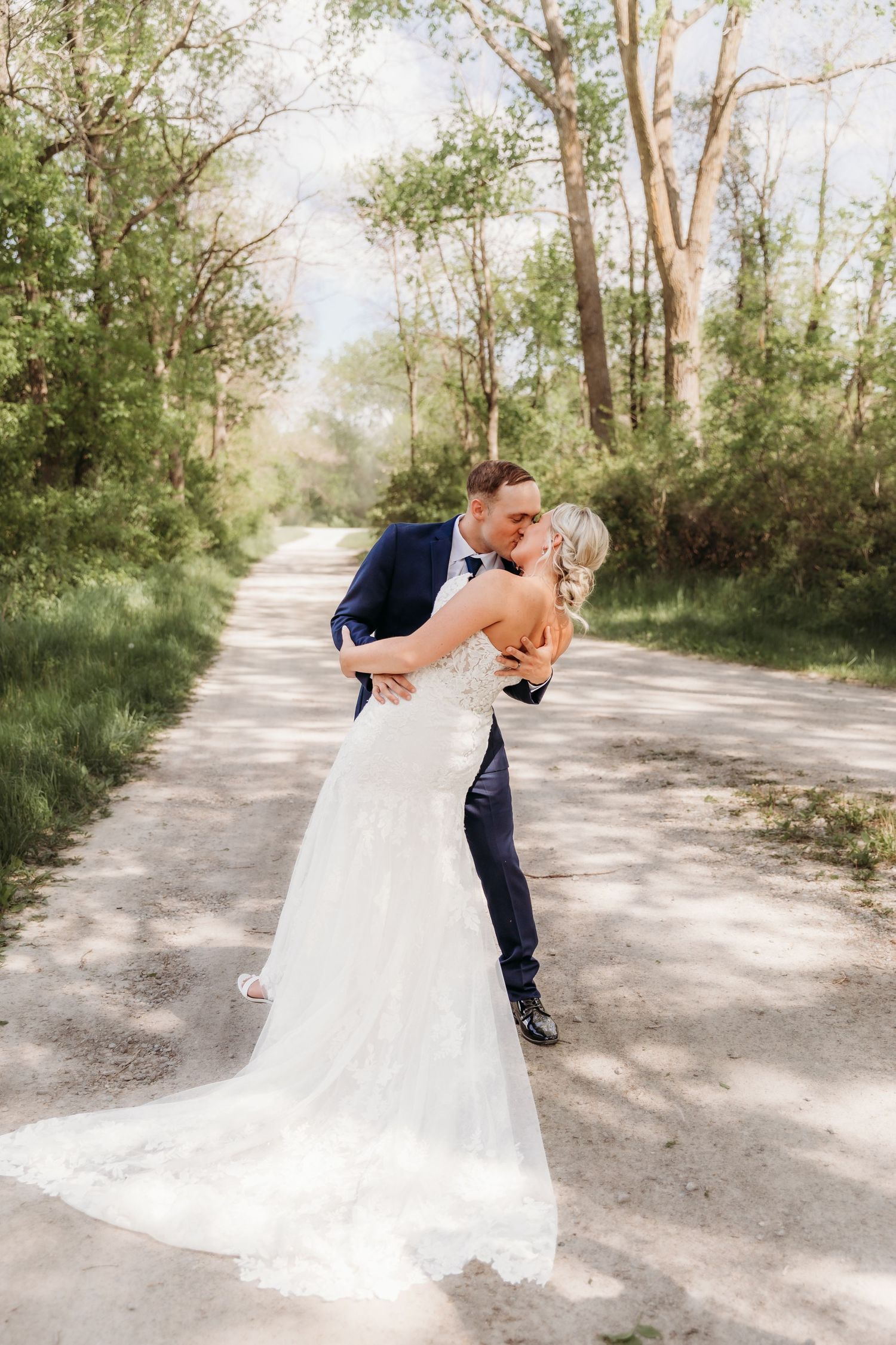 Romantic wedding couple sharing intimate moments on a sunlit path surrounded by trees.