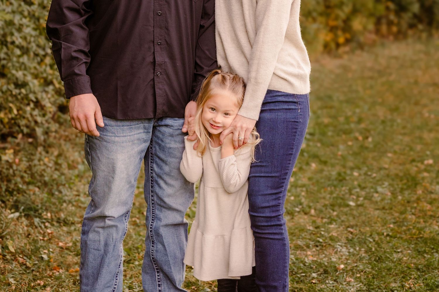 Candid family moment outdoors with child holding parents' hands in autumn setting.