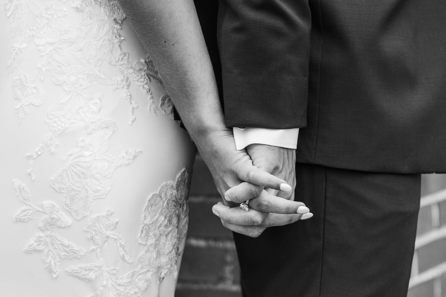 Close-up view of newlyweds holding hands showing wedding rings and formal attire details.