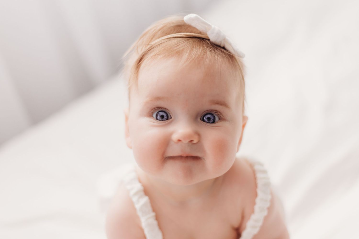 Close-up portrait of smiling baby wearing white straps against light background.