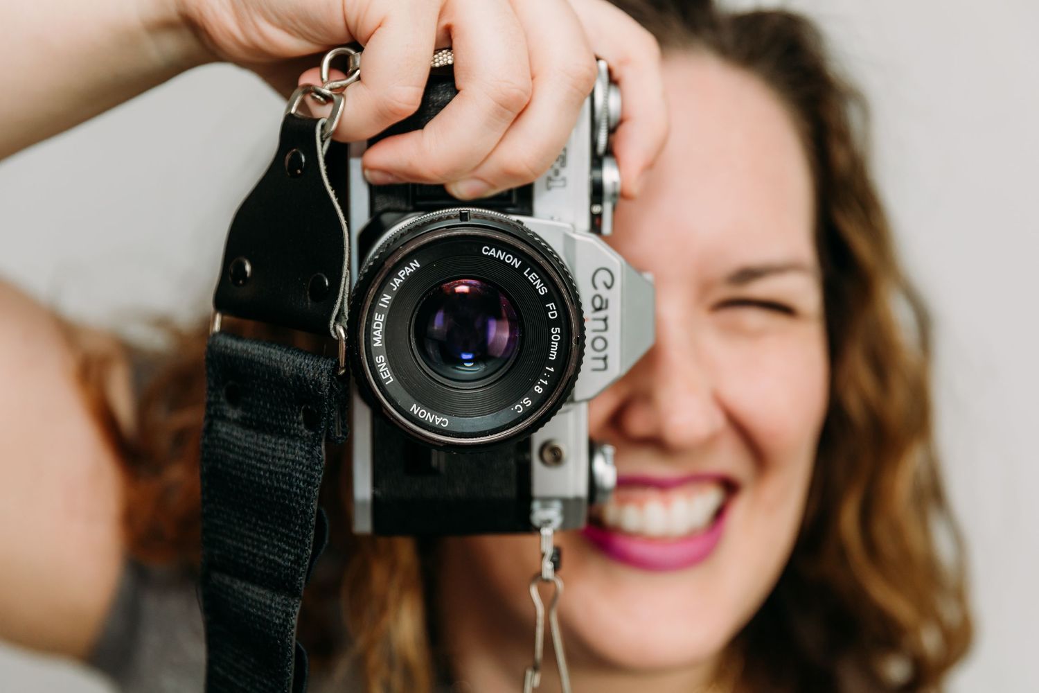Person holding vintage film camera and smiling while taking photos in natural light.