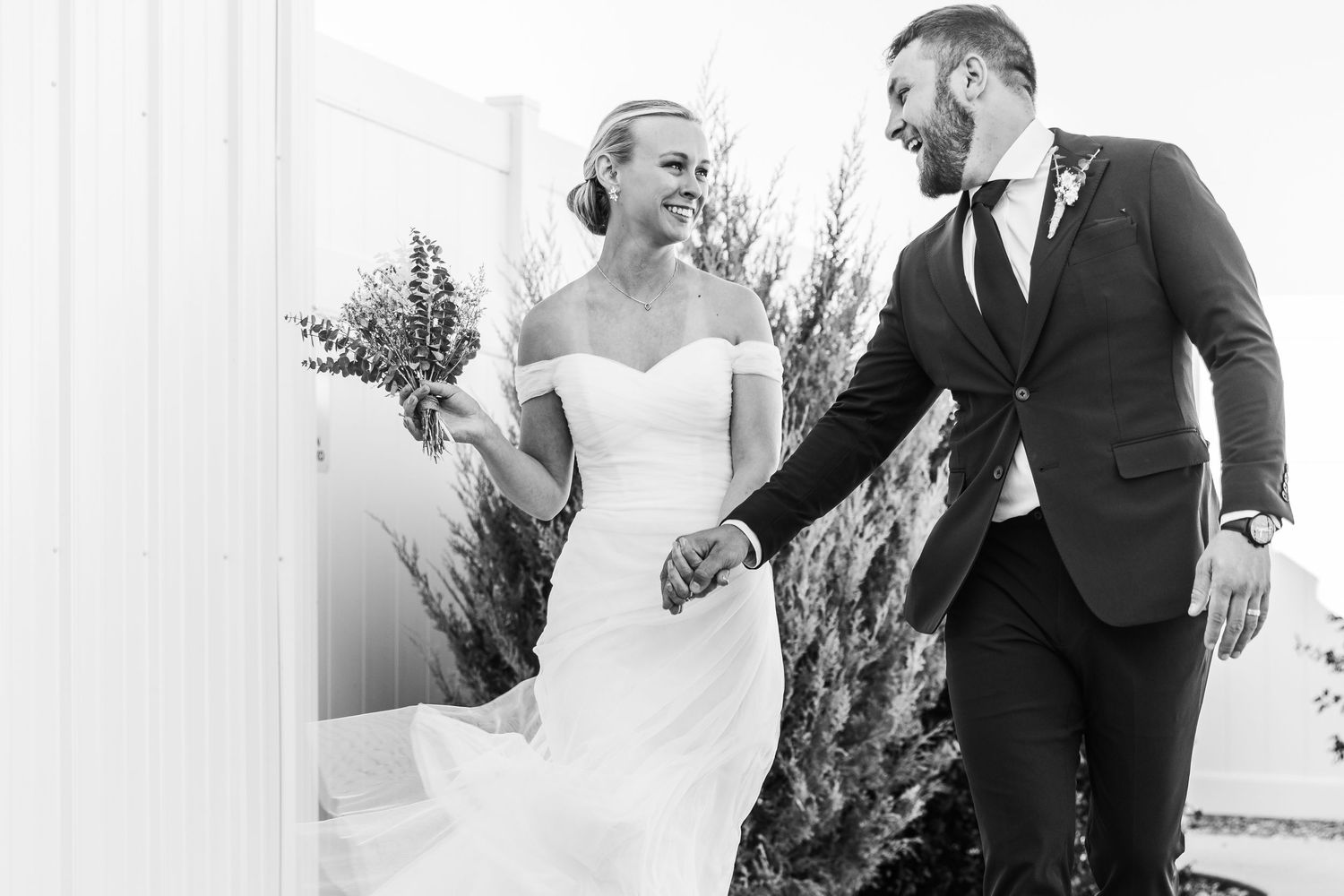 Black and white photo of newlyweds sharing a joyful moment in wedding attire.