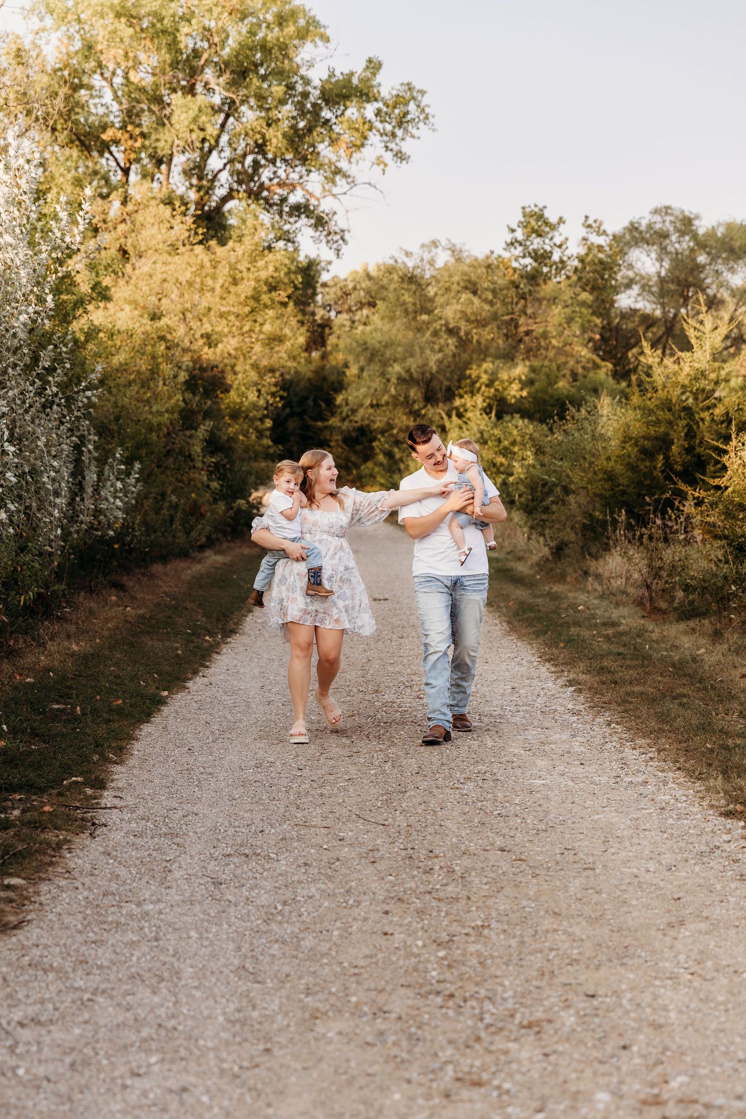 Family plays and dances together on a sunlit gravel path surrounded by autumn trees.