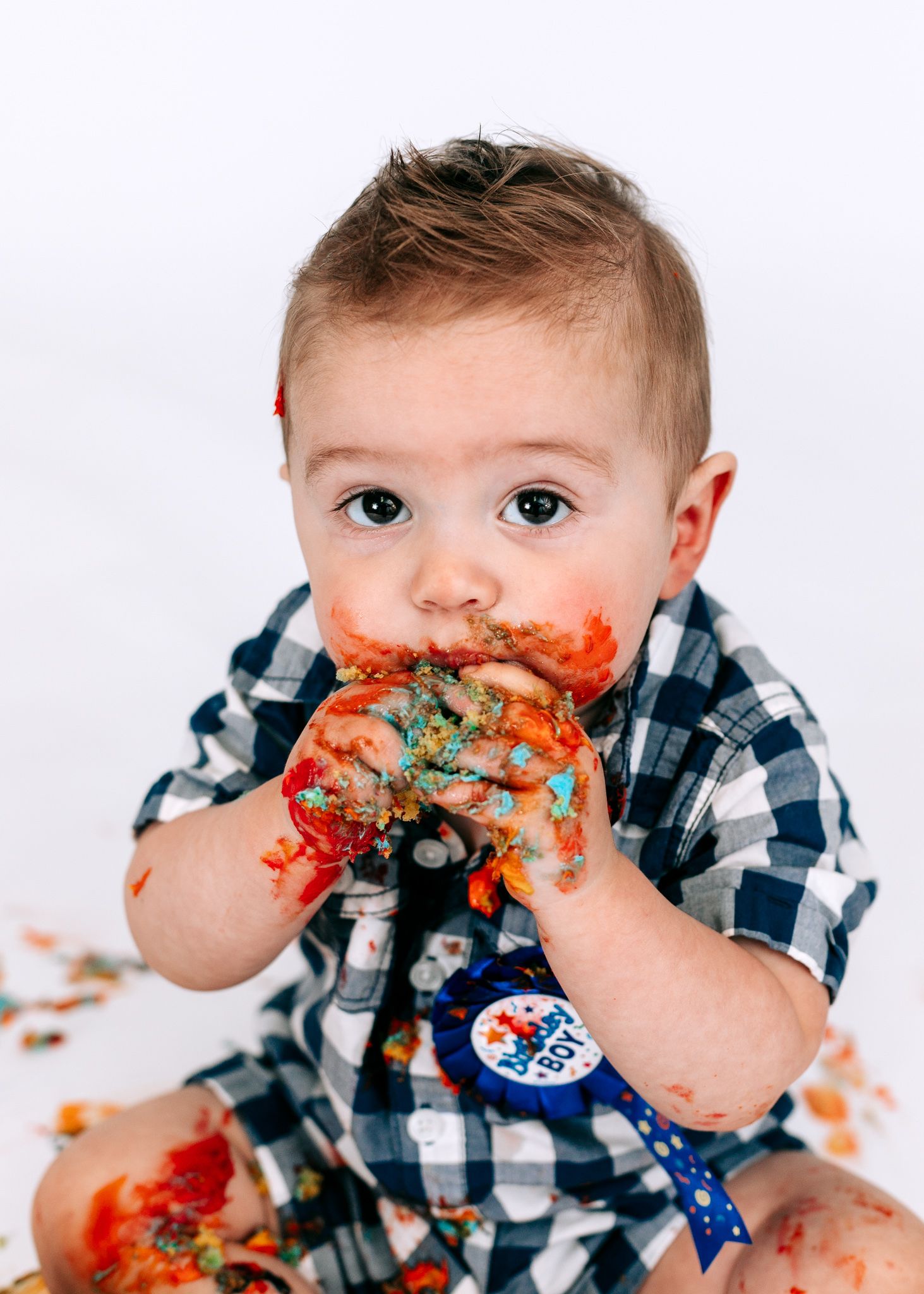 A cute baby boy with cake smashed on his face during a first birthday smash cake session.